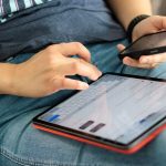 Pessoa usando um tablet e um smartphone em ambiente interno, representando o acesso digital a serviços e informações.