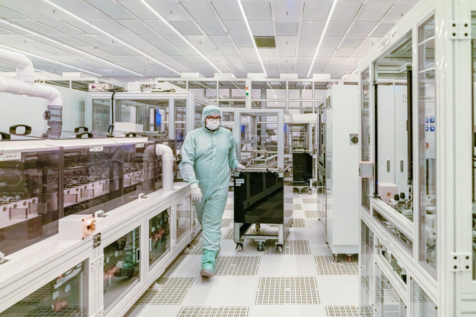 Cientista usando roupa protetora caminha por uma sala limpa de alta tecnologia.