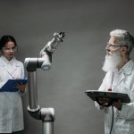 Dois pesquisadores trabalham com um braço robótico em um laboratório de tecnologia.