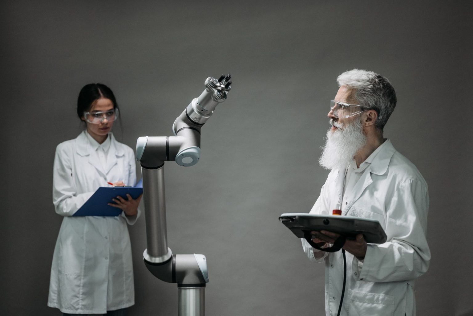 Dois pesquisadores trabalham com um braço robótico em um laboratório de tecnologia.