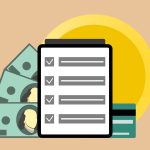Tablet com marcas de verificação ao lado de cédulas de dólar e um cartão de crédito.